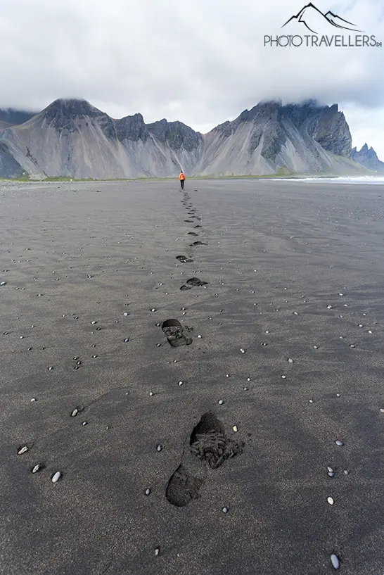 Fußspuren an einem schwarzen Strand in Island, die ins Bild führen