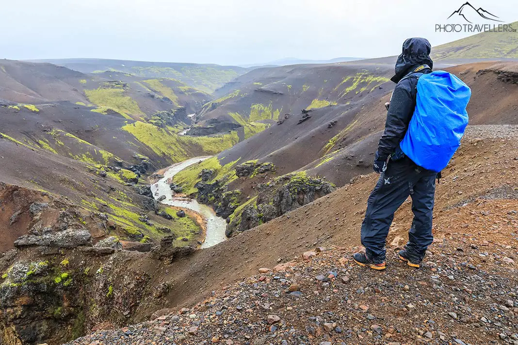 Reiseblogger Flo in Regenklamotten und mit Rucksack an einem Canyon in Island