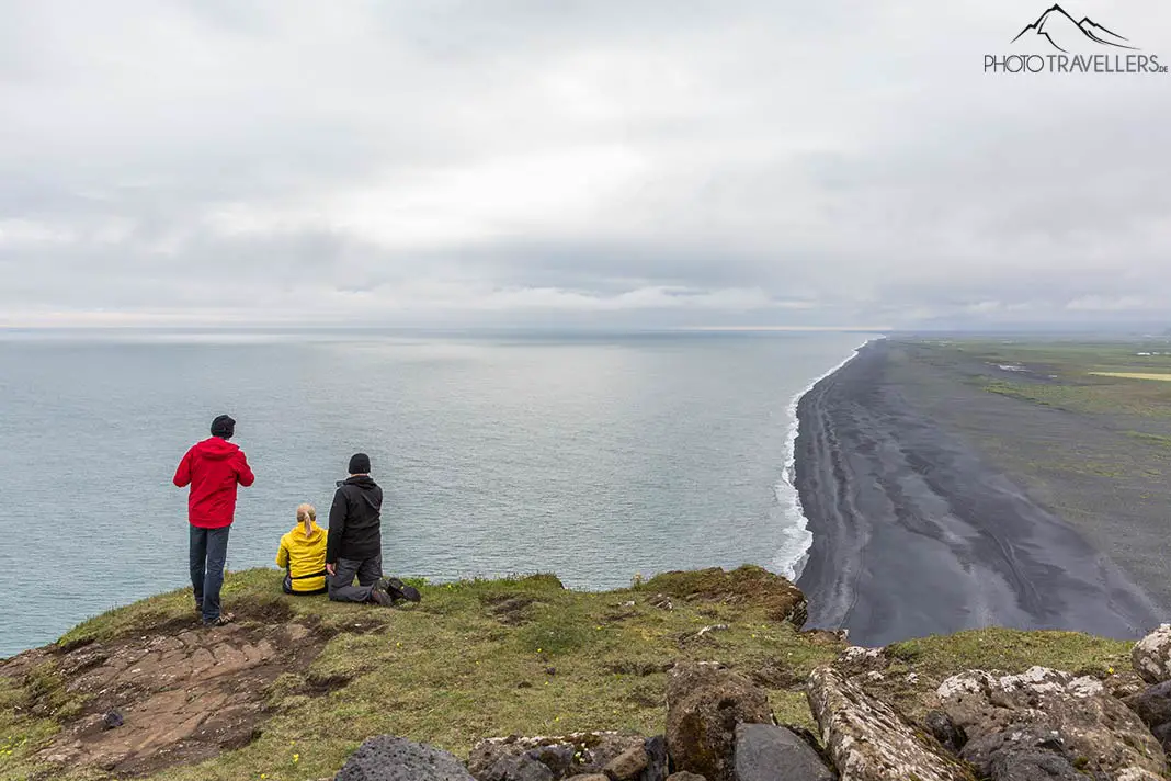 Tourists look from a cliff over the coast of Dyrhólaey