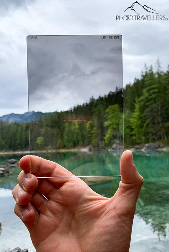 Ein Lee-Grauverlaufsfilter in der Stärke 0.9 soft, in einer Hand gehalten vor einem Bergsee