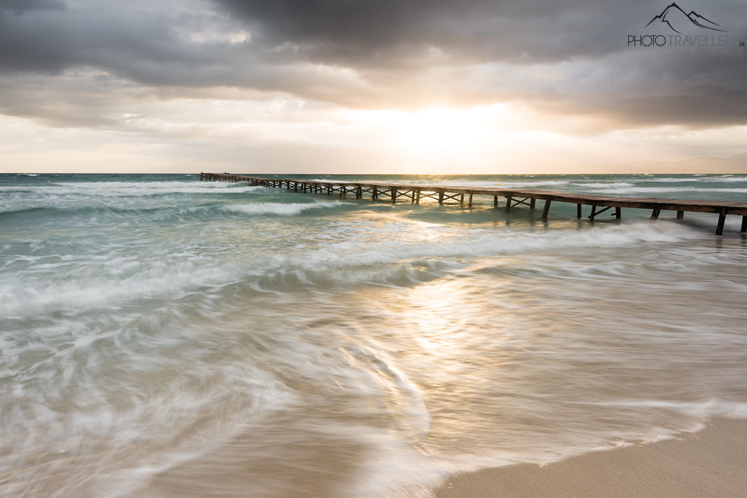 Ein langer Holzsteg im Meer im Abendlicht an der Playa de Muro auf Mallorca