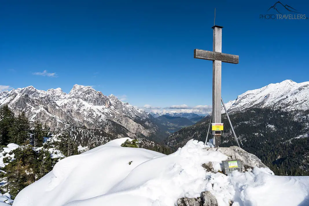 The summit cross on the Litzlkogel in winter with a view of Hintersee lake