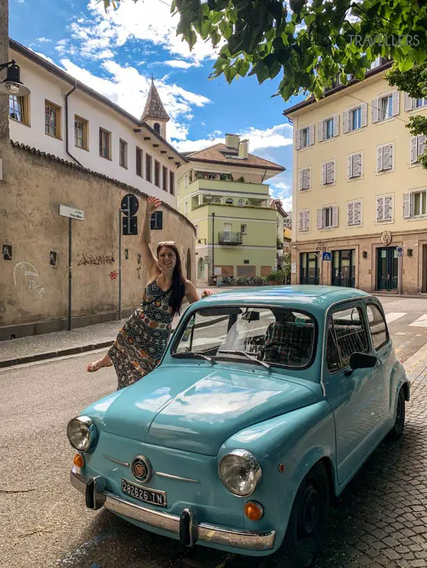 Reisebloggerin Biggi Bauer vor einem alten blauen Auto mitten in Bozen