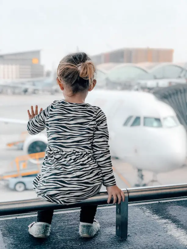 Kind beobachtet Flugzeug durch die Fensterscheibe am Flughafen