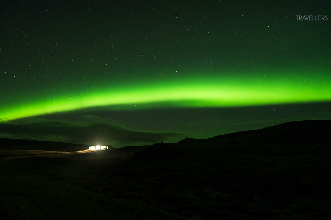 Ein Polarlicht über einer beleuchteten Hütte auf Island