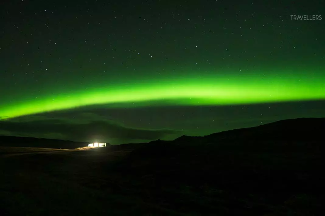 Ein Polarlicht über einer beleuchteten Hütte auf Island