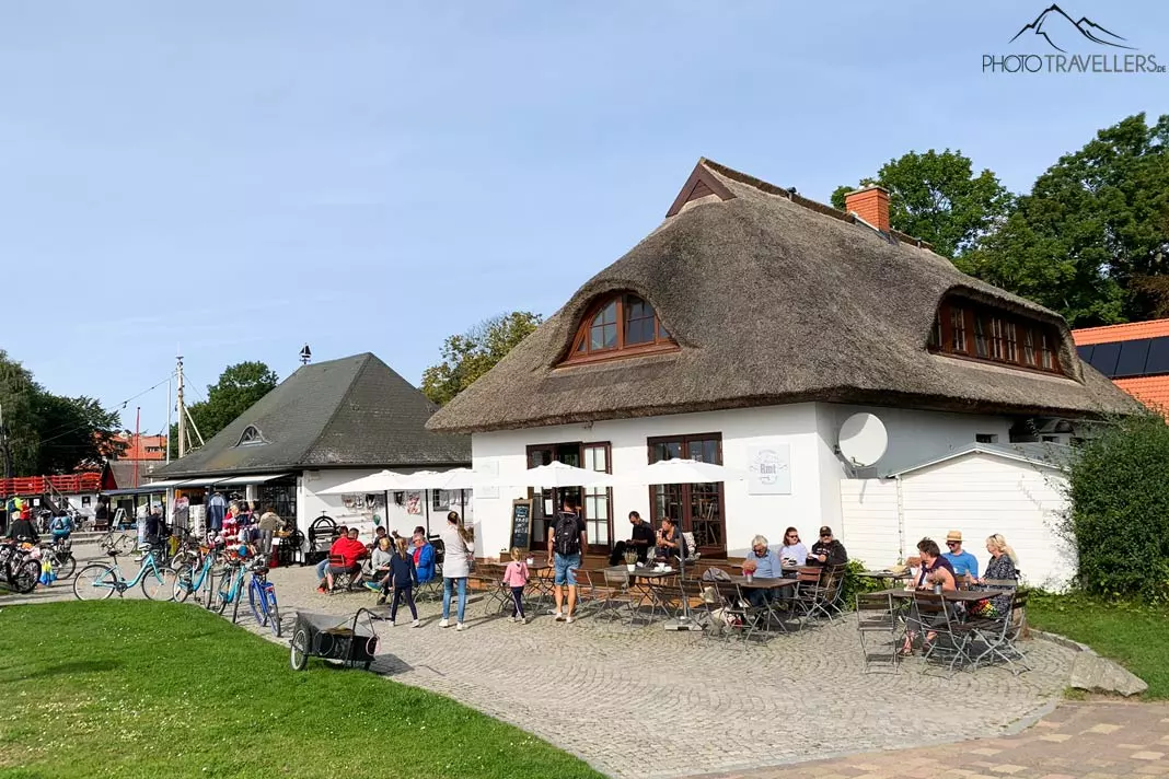 Menschen sitzen vor einem Café im Hafen vom Ort Kloster auf Hiddensee