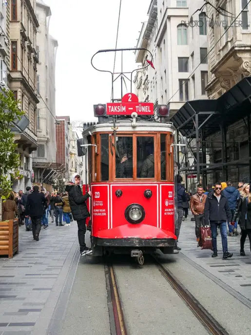 A young man hangs on the red streetcar in the Galata district