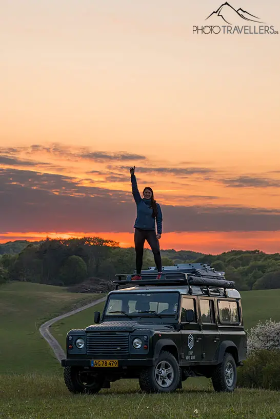 Reisebloggerin Biggi Bauer auf dem Dach eines Land Rovers im Abendlicht
