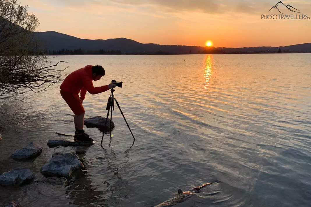 Reiseblogger und Fotograf Florian Westermann am Abend mit Kamera und Stativ im Wasser des Kochelsees