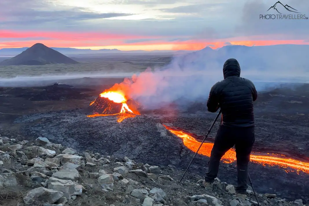 Profifotograf Florian Westermann mit Stativ und Kamera in Island vor einem glühenden Vulkan