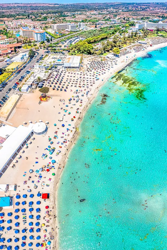 Blick aus der Luft auf den Nissi Beach in Zypern - der Strand ist voll an Liegen und Sonnenschirmen