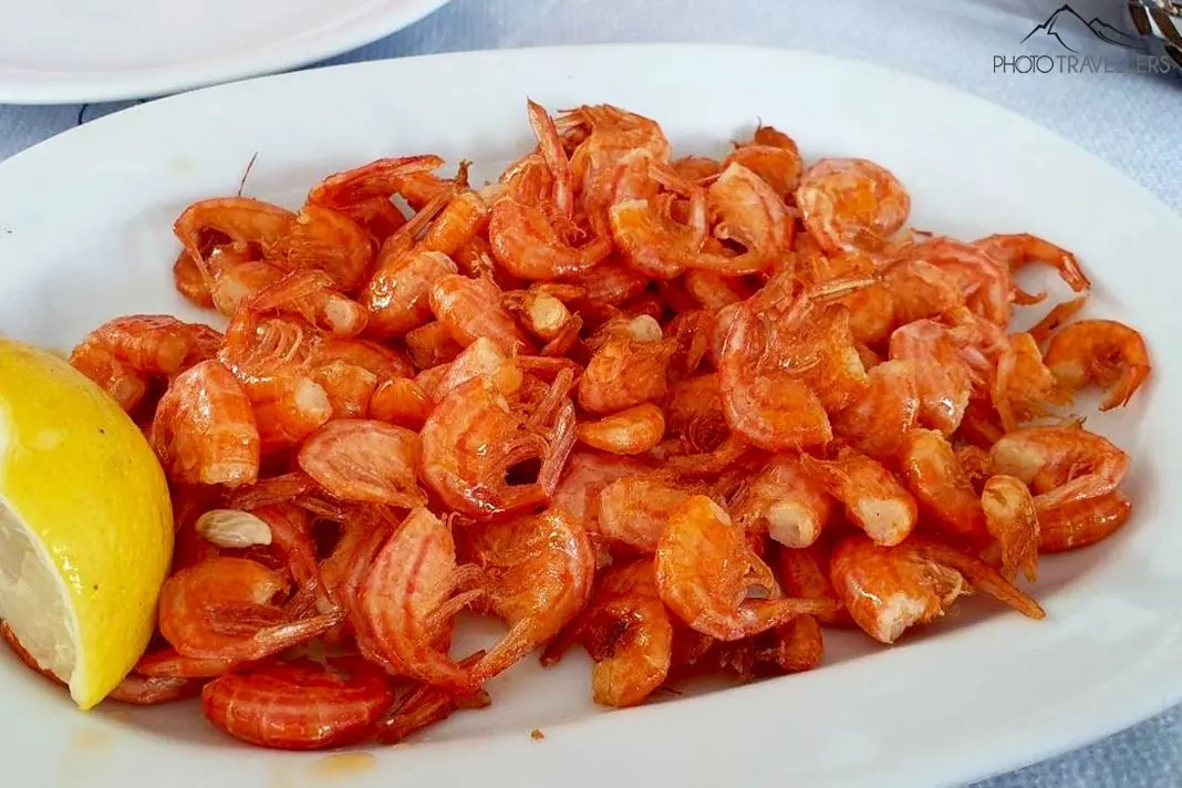 Viele kleine orangefarbene Shrimps zieren einen Teller mit Zitrone