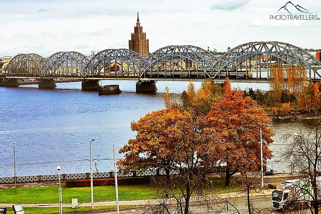 Eisenbahnbrücke über den Fluss Daugava in Riga mit Laubbaum im Vordergrund