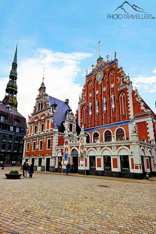 Der Turm der Petrikirche ragt über die zwei roten Backsteinfassaden des Schwarzhäupterhauses in Riga