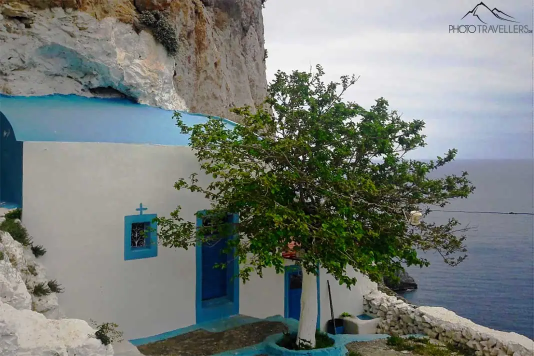 Ein Baum steht vor der weiß-blauen Kapelle Agios Fotis an der Felswand