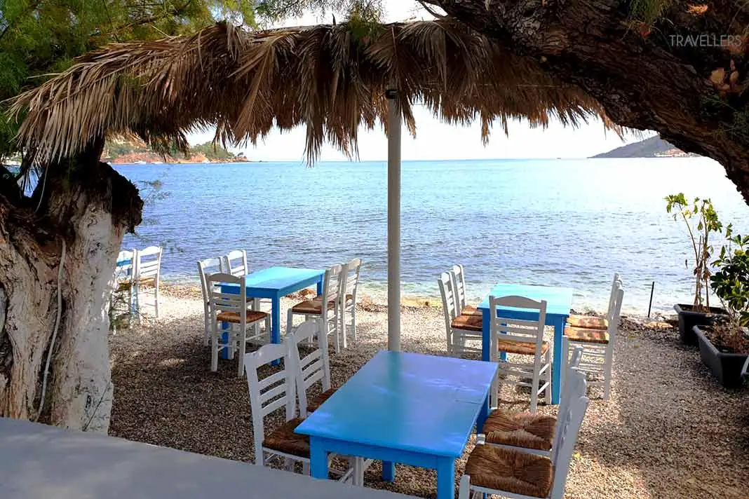 Tische und Stühle stehen unter einen Baum am Strand von Alinda