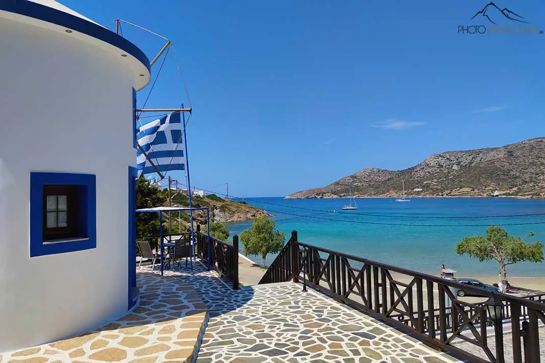 Griechenlandflagge weht vor einem weißen Haus direkt am türkisblauen Meer