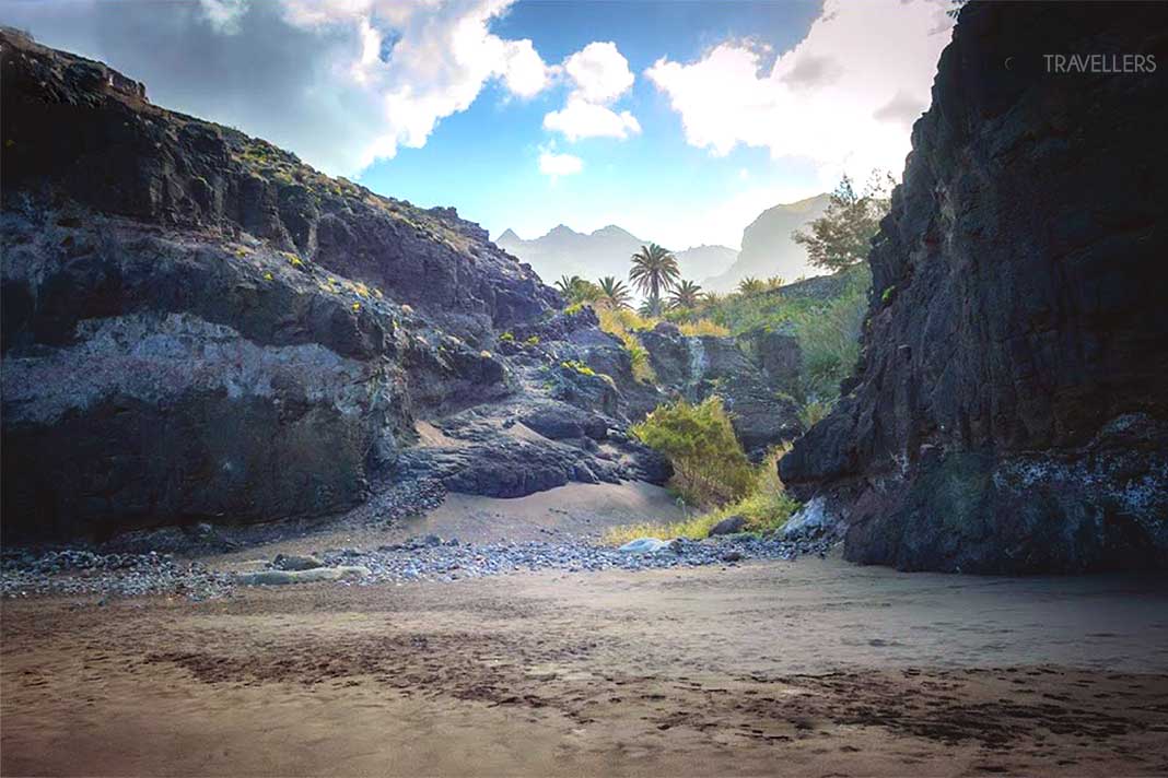 Der Sandstrand von Güigüi wird von Felsen und Palmen umrahmt