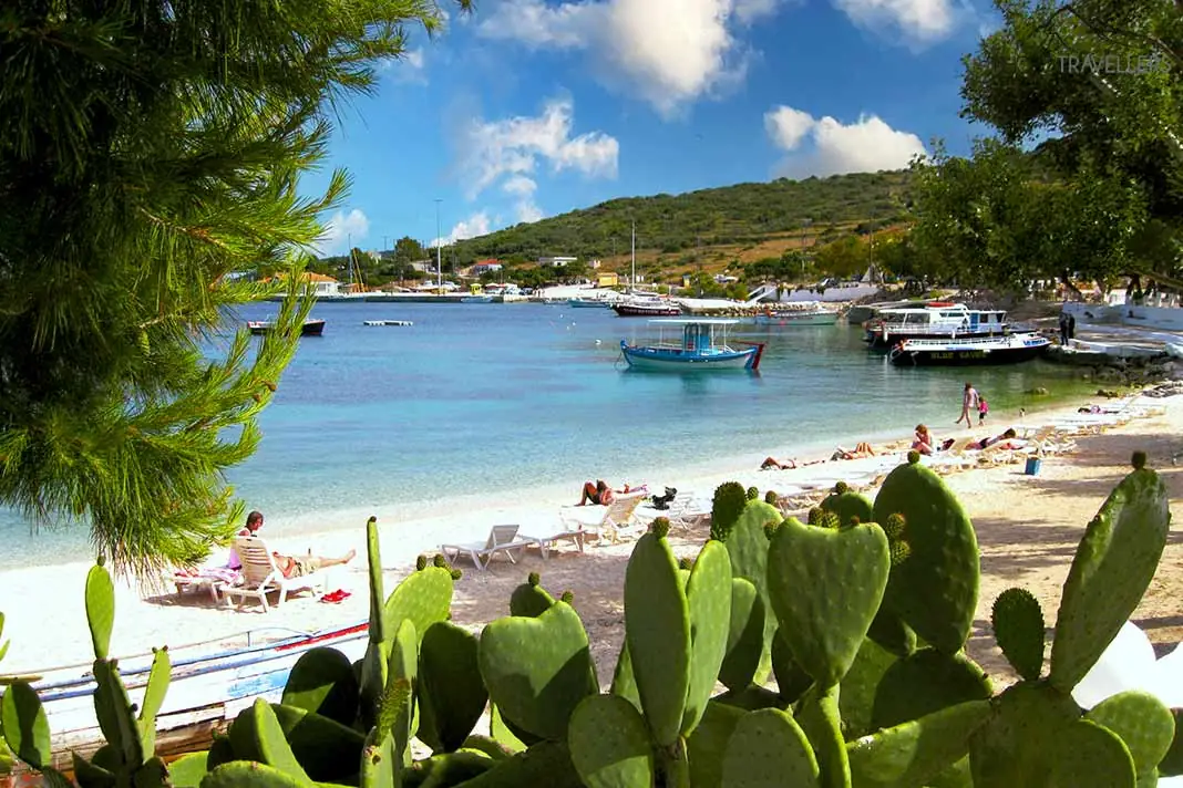 Badegäste und kleine Boote säumen den mit Kakteen bewachsenen Strand in Agios Nikolaos