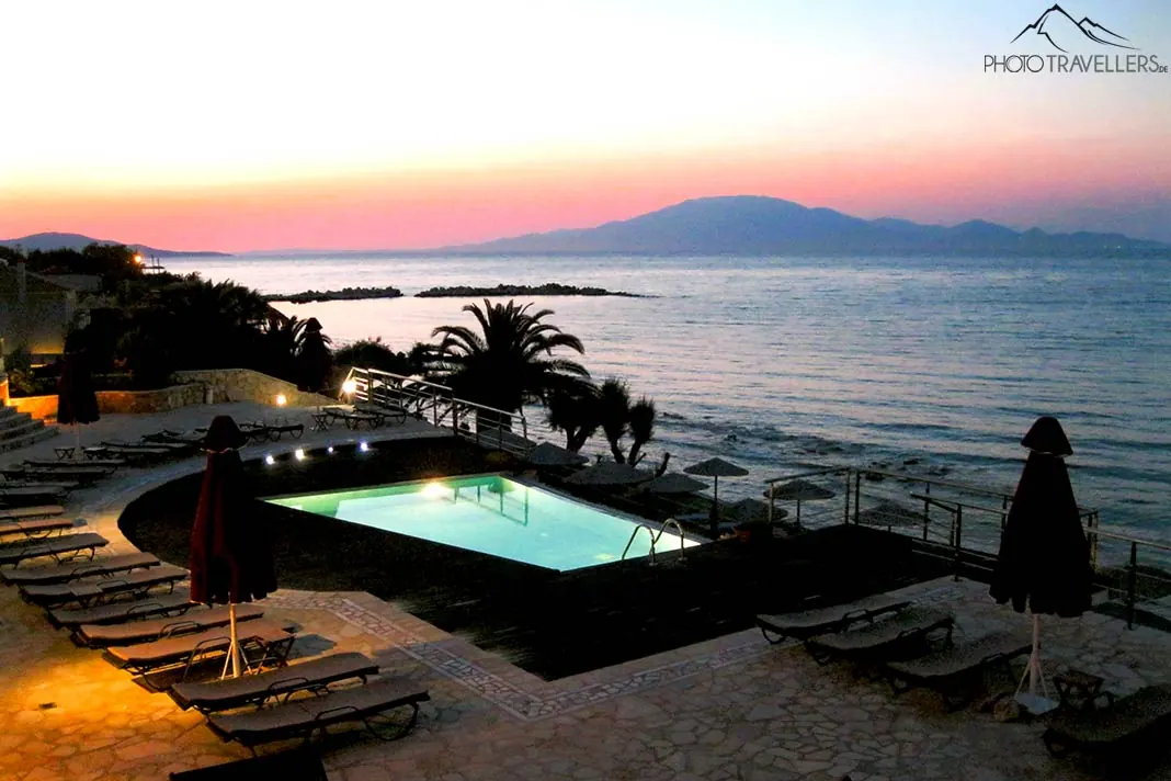 Beleuchteter Hotelpool mit dem Abendrot über dem Meer im Hintergrund 