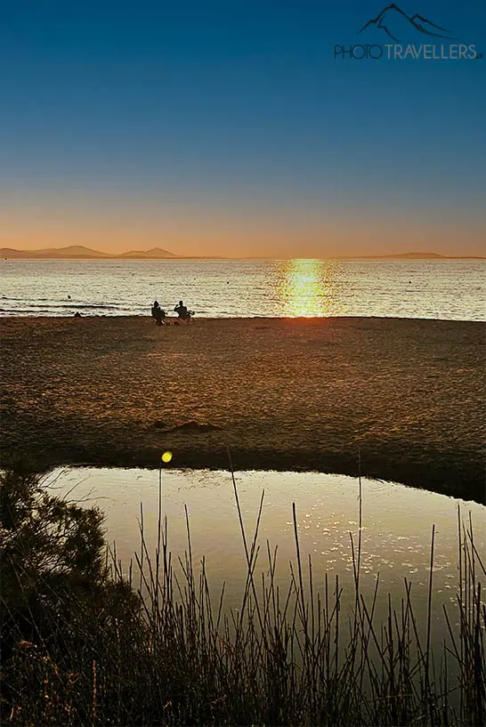 Zwei Menschen beobachten am Strand den Sonnenuntergang am Plaka Beach