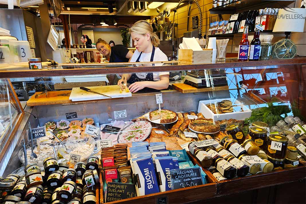 Eine blonde Verkäuferin bereitet Feinkost an ihrem Stand in der Markthalle in Helsinki zu