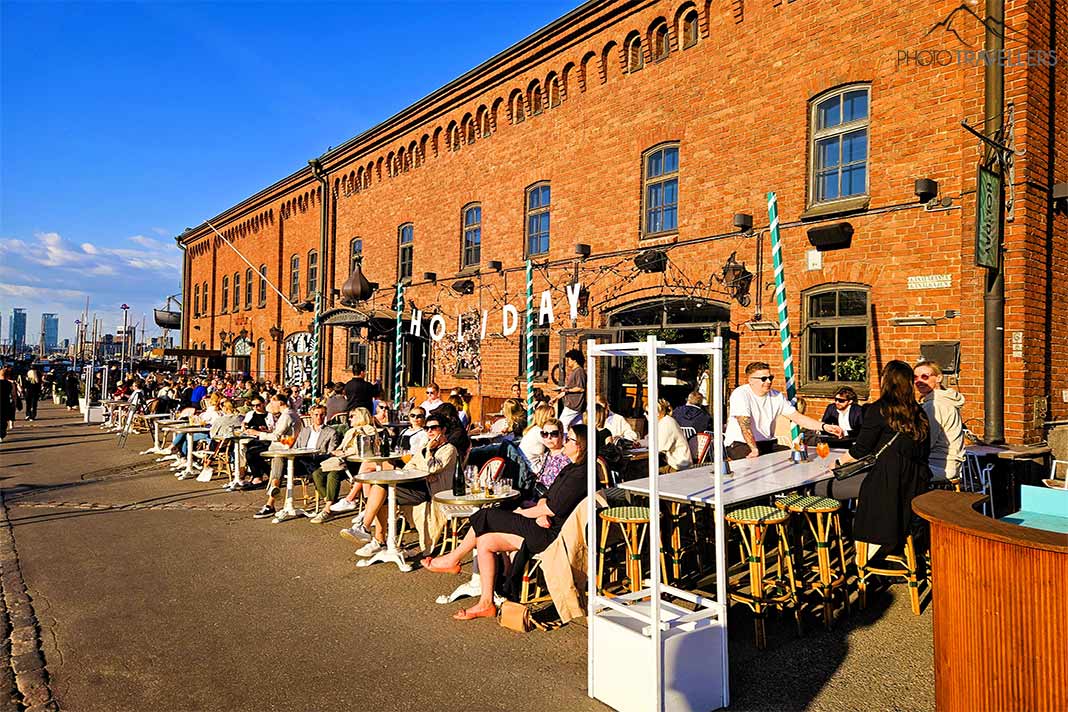 Viele Besucher sitzen in den Bars vor den Backsteingebäuden am neuen Hafen in Helsinki