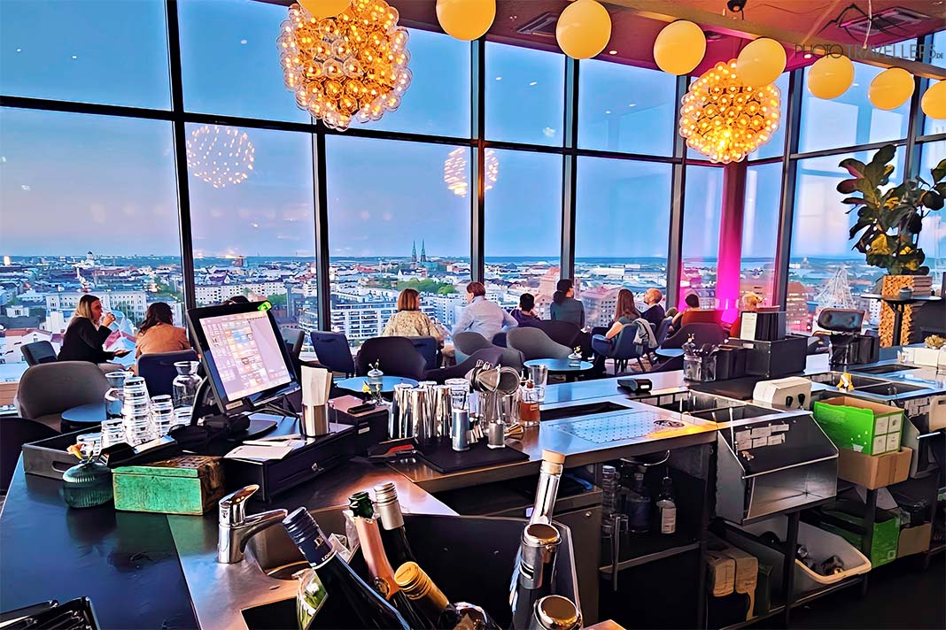 Die Gäste im Sky Room schauen aus der verglasten Rooftopbar auf Helsinki herab