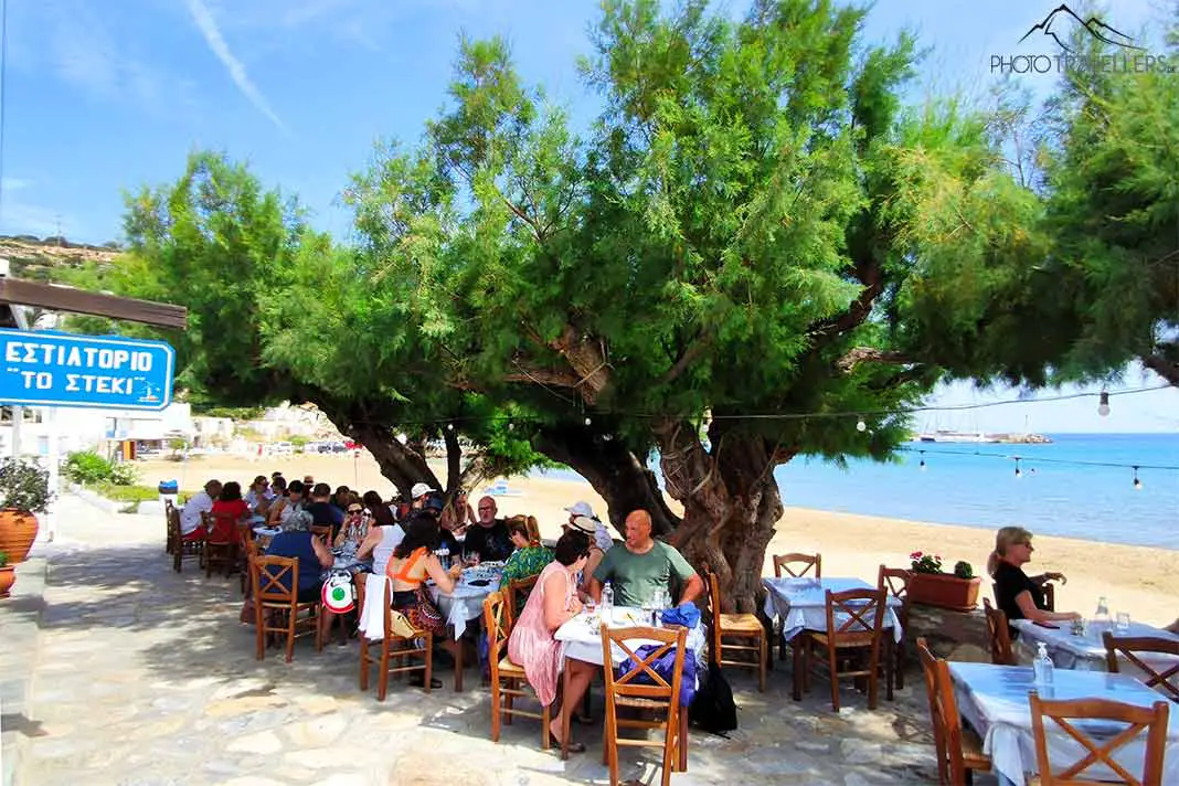 Viele Gäste sitzen an den Tischen unter Bäumen einer Taverne in Platis Gialos