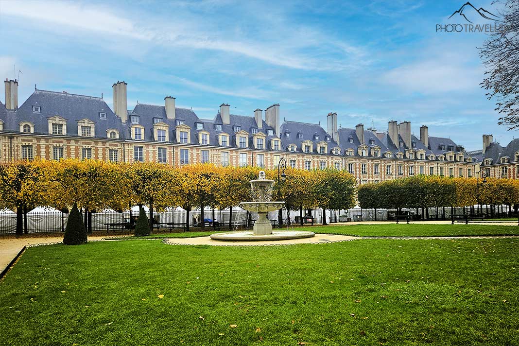 Eine Skulptur ziert den Parc des Vosges mit einer Laubbaumallee und Backsteingebäuden im Hintergrund