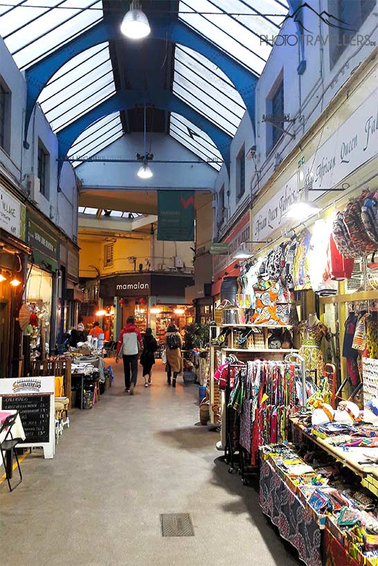 Einige Besucher schlendern durch die mit bunten Waren ausstaffierten Stände in der Markthalle in Brixton