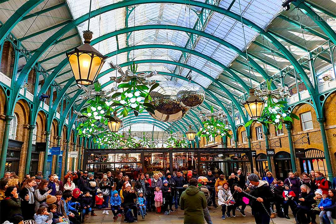 Unter dem gewölbten Glasdach des Covent Garden Markets bestaunen Gäste das Treiben der Straßenkünstler