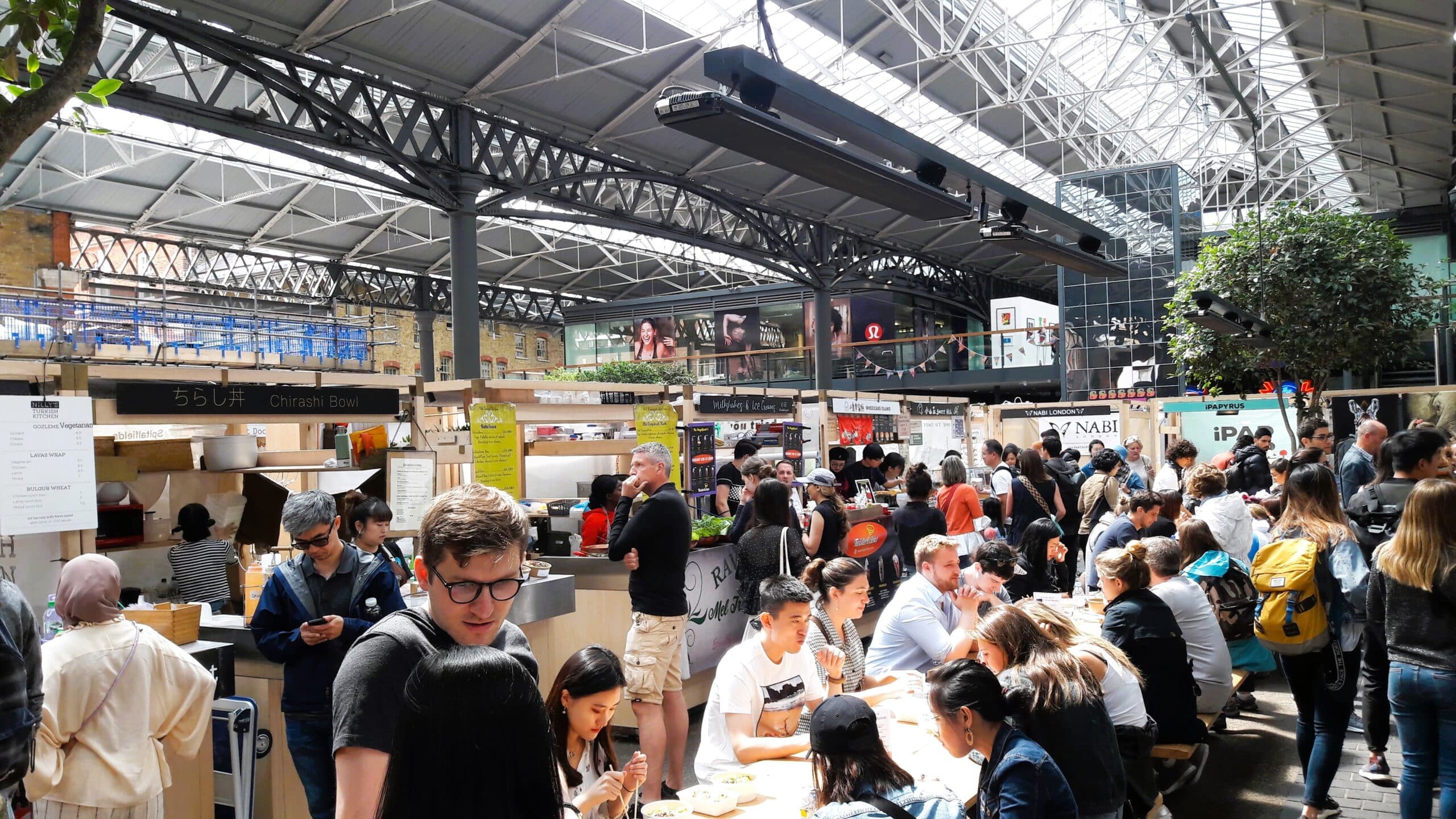 Viele Besucher des Spitalfield Markets essen an den Tischen im Gastrobereich