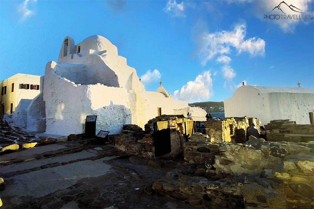 Vor der weißen Kuppelkirche Paraportiani sind Reste der antiken Stadtmauer zu sehen