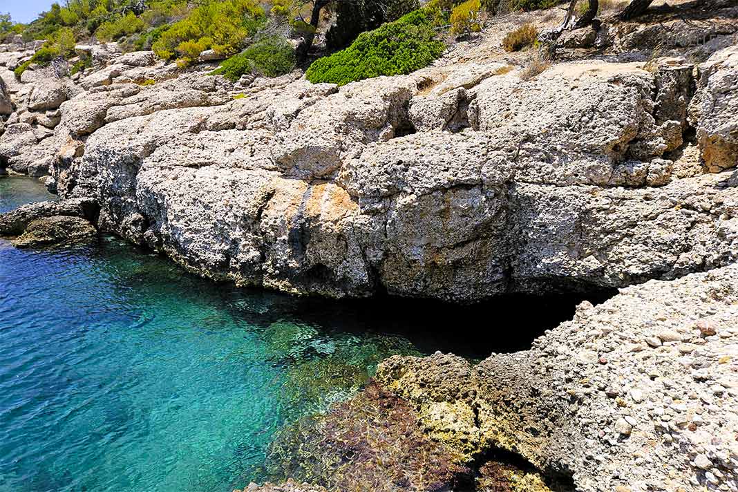 Der Eingang zur Bekiris-Höhle liegt unter einem Felsplateau vor türkisblauem Wasser