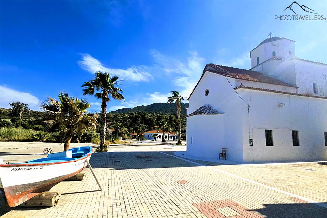 Vor der gleichnamigen Kirche in Agios Georgios stehen Palmen und ein Holzboot