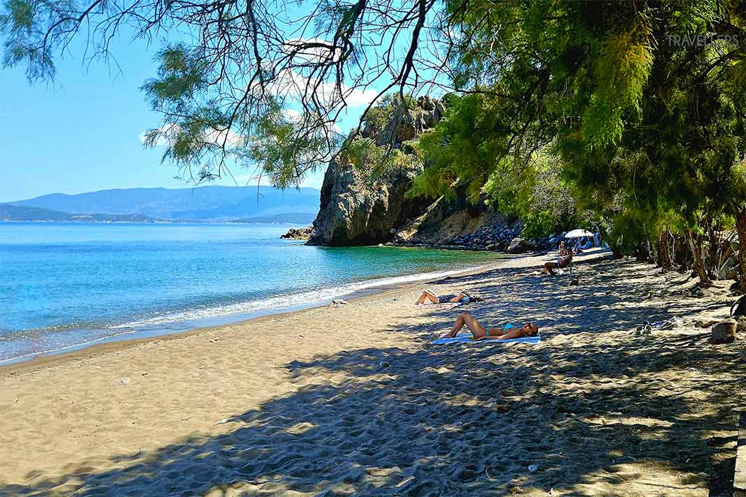 Badegäste liegen am Sandstrand von Limnionas umgeben von Felsen und Pinien