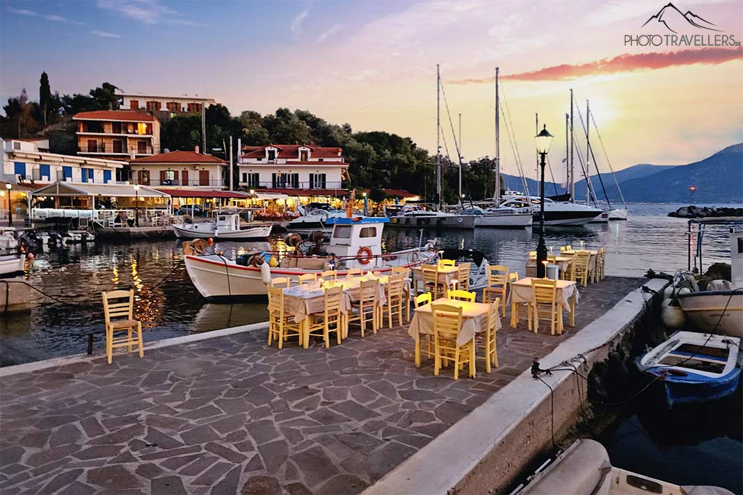 Stühle einer Taverne stehen im Sonnenuntergang neben Booten im Hafen von Vathi