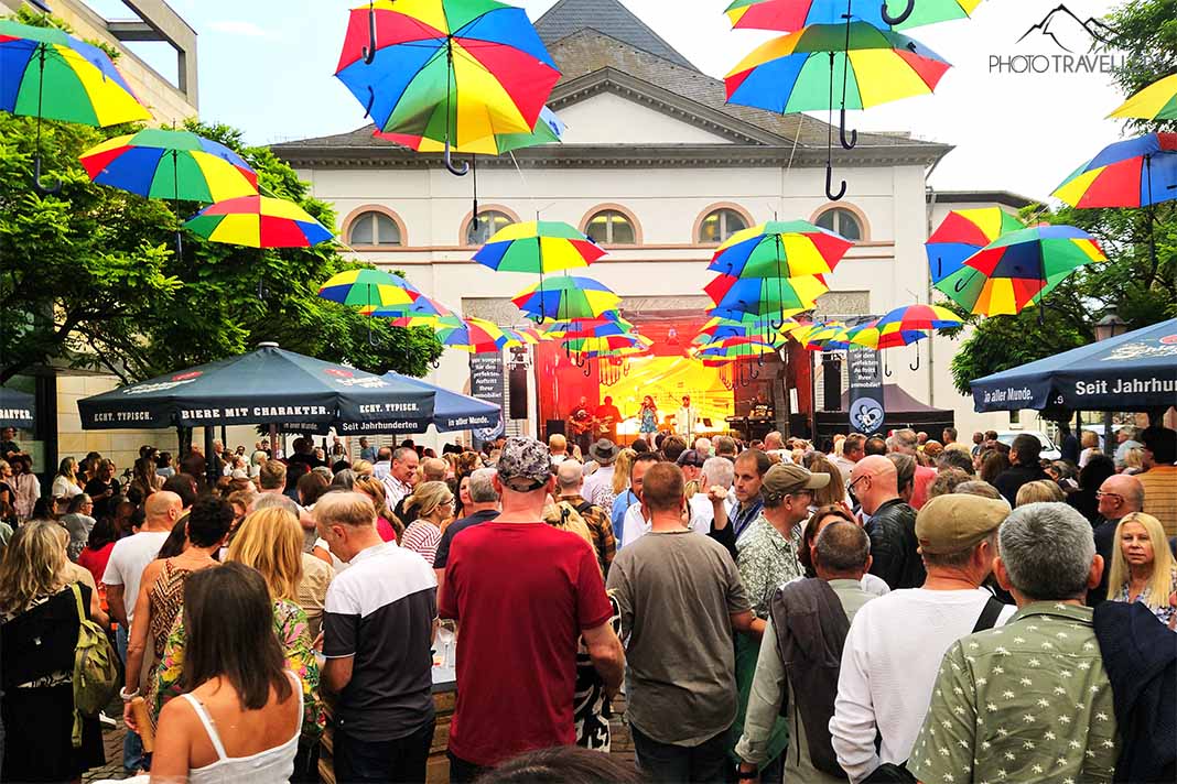 Viele Menschen stehen vor einer Musikbühne mit bunten Regenschirmen an Leinen gespannt vor dem Stadttheater Aschaffenburg