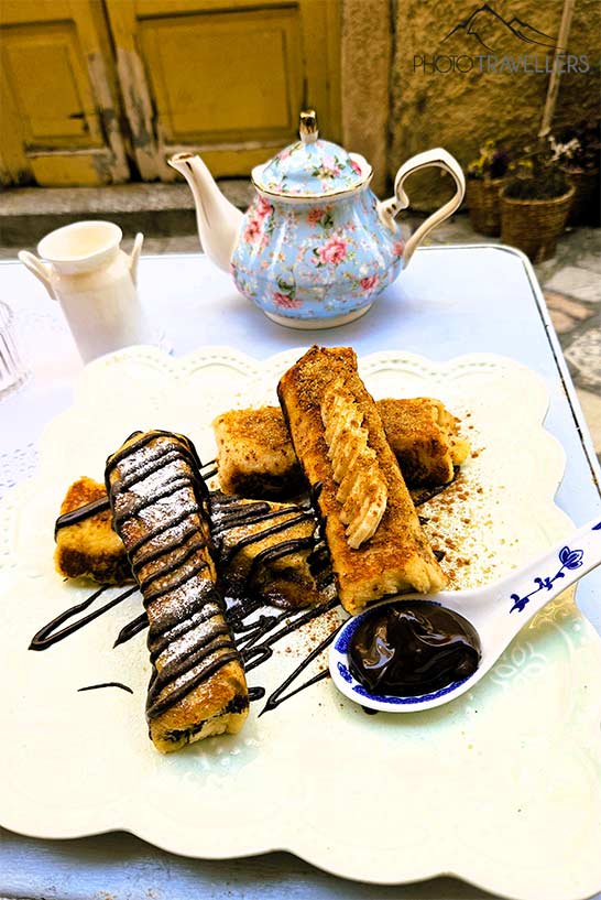 Auf einem edlen Service mit hellblauer Teekanne liegt süßes Gebäck und ein Löffel voller Schokolade