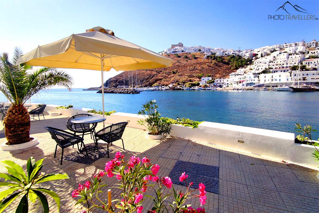 Sonnenschirm und Stühle stehen auf einer Terrasse mit Blick auf die Marina von Pera Gialos