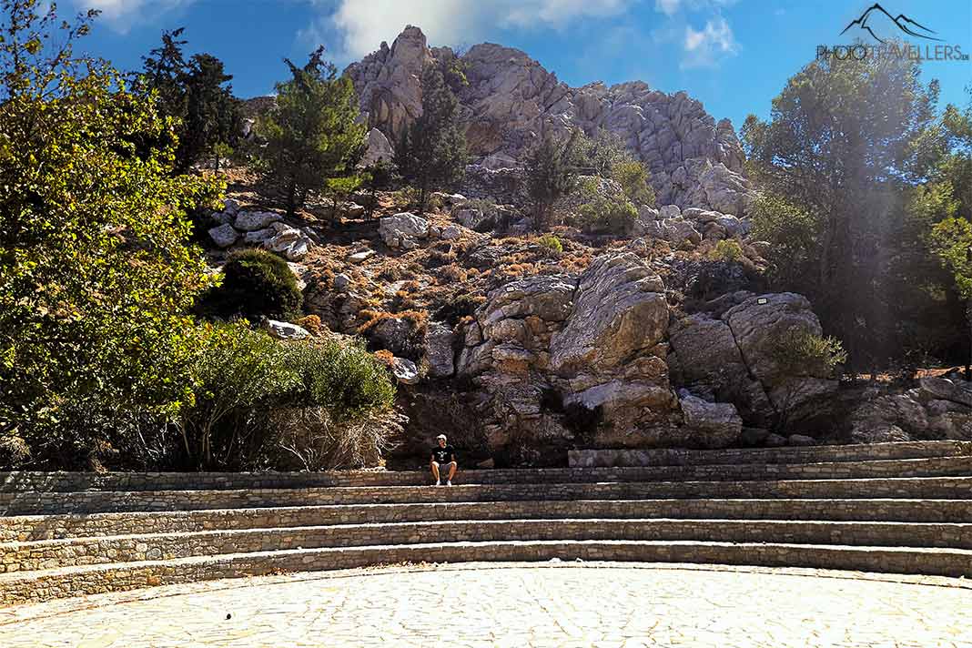 EIn Mann sitzt auf den Treppen des Amphitheaters Charkadio vor einem Berg