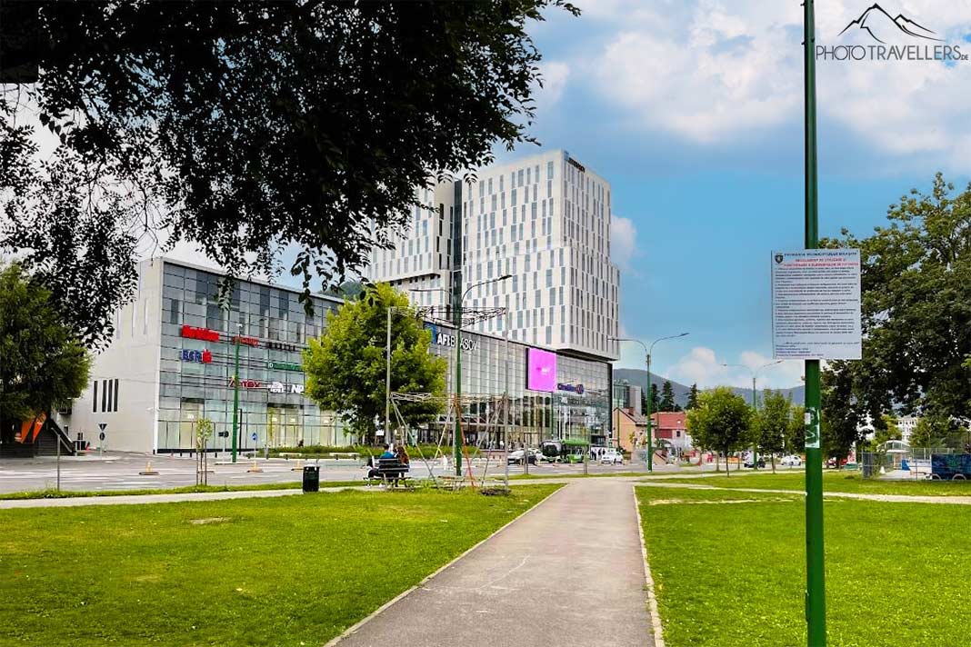 Ein Park mit Rasenfläche und Bäumen vor einem großen Einkaufscenter in der Neustadt von Brasov