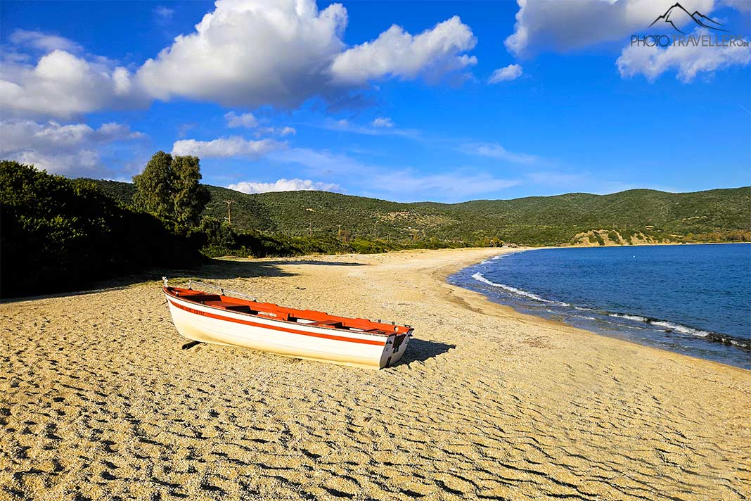 Ein kleines Holzboot liegt am Sandstrand von Ladhario mit Bäumen im Hintergrund