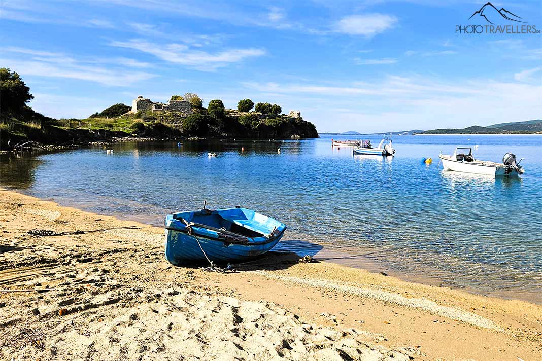 Ein kleines blaues Holzboot liegt in der Bucht von Toroni mit den Ruinen der alten Festung im Hintergrund