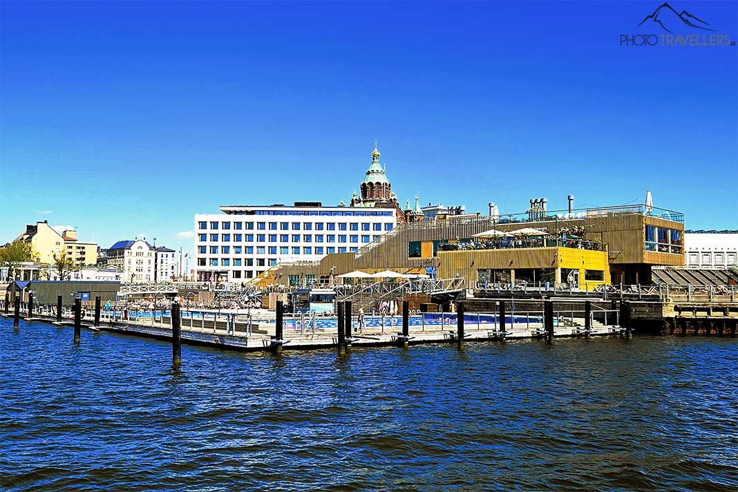 Becken des Allas Meerespools im Hafen von Helsinki mit Holz- und Geschäftshaus im Hintergrund