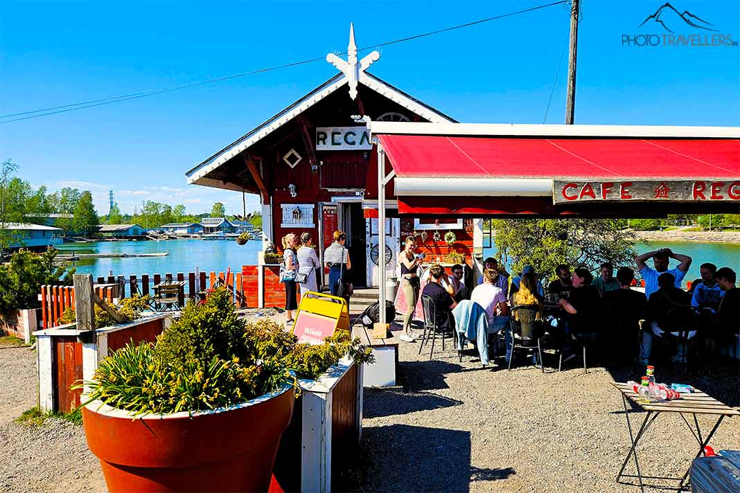 Das Cafe Regatta ist eine rote Holzhütte am Meer mit vielen Menschen vor einem überdachten Außenbereich