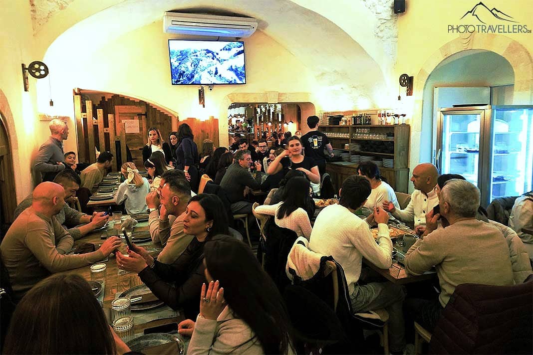 Viele Menschen sitzen an den Tischen eines Lokals mit Gewölbedecke in Brindisi
