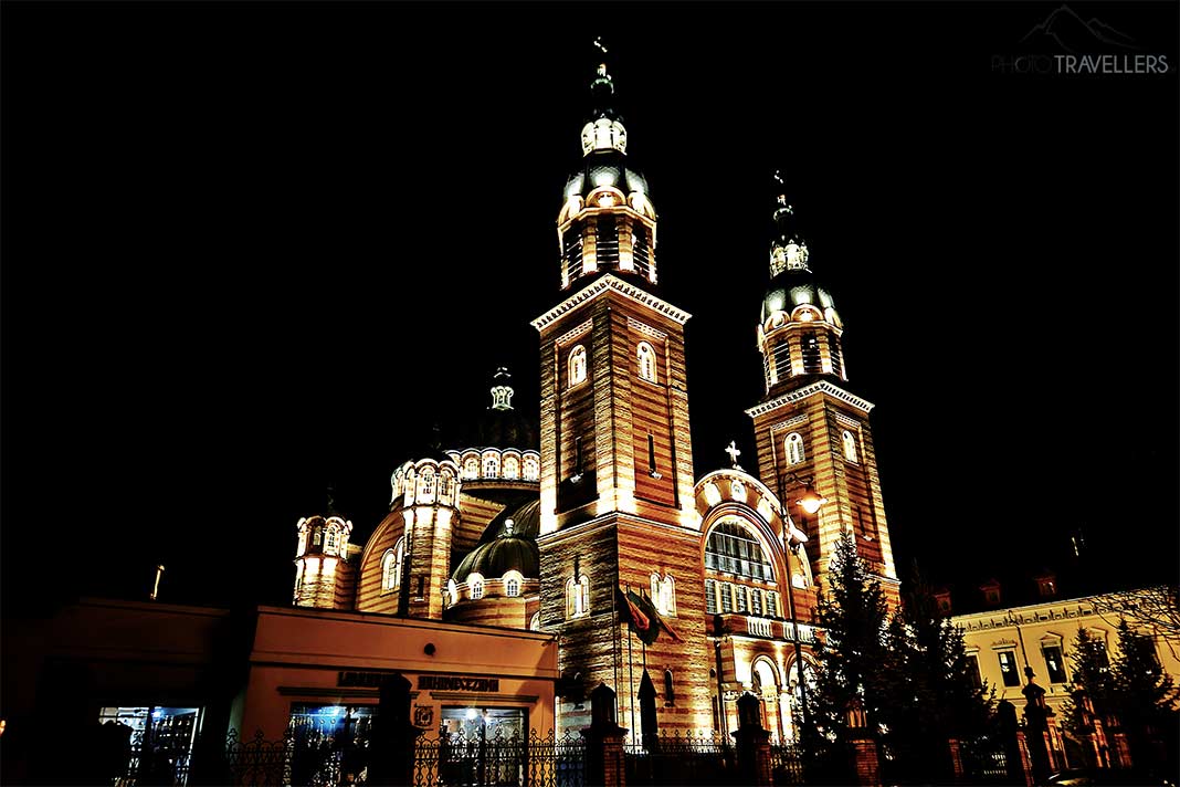 Beleuchte, goldbraune Fassade der Kathedrale von Sibiu mit zwei Türmen und Kuppel bei Nacht